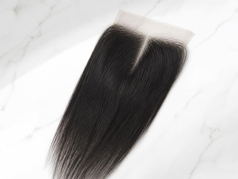 A 4x4 human hair lace closure with a middle part laid flat on white marble.