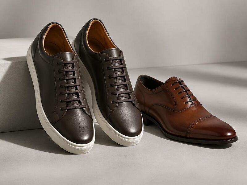 Dark brown leather men's sneakers next to a tan cap-toe oxford dress shoe.