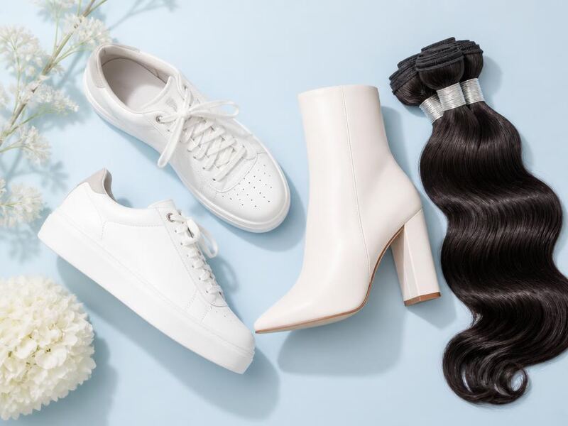 New season white sneakers, a white heeled boot and a wavy human hair bundle on a pale blue backdrop.